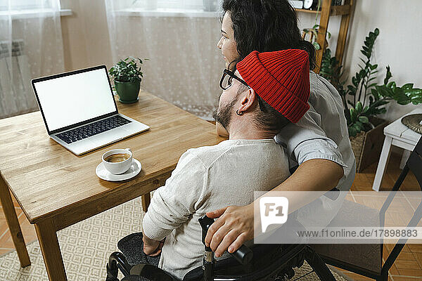 Woman sitting by boyfriend with disability looking at laptop on table