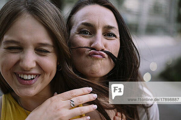 Playful woman making mustache with hair of friend