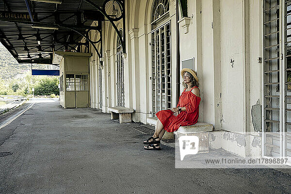 Senior woman in red dress sitting on bench at railroad station