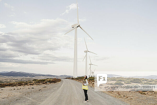 Ingenieur steht auf unbefestigter Straße neben Windkraftanlagen im Windpark