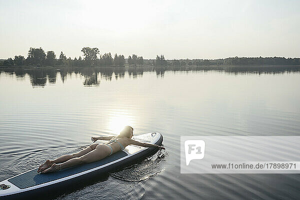 Woman paddling with hand lying on paddleboard at sunset