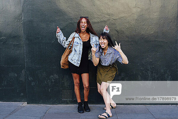 Cheerful woman enjoying with friend standing in front of wall