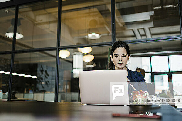 Young woman having fruits at laptop in office