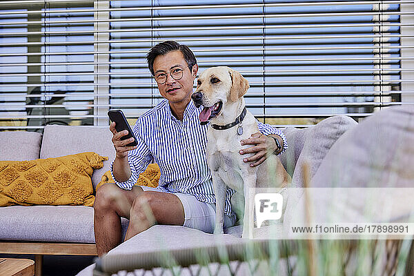 Lächelnder reifer Mann mit Hund sitzt auf dem Sofa
