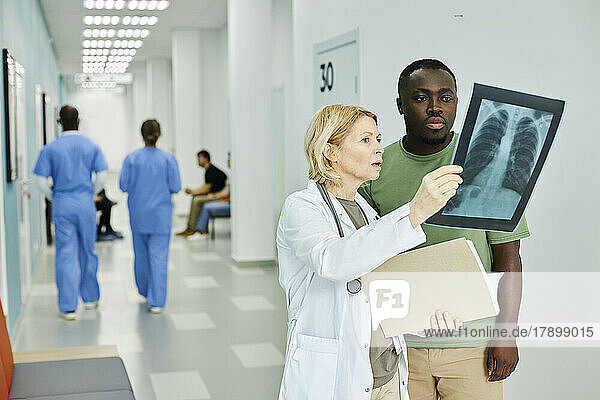 Doctor explaining X-ray image to patient standing in hospital corridor