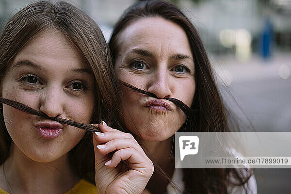 Two women having fun making mustache with hair