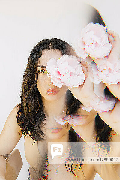 Multiple exposure of young woman holding pink flower over eye
