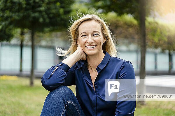 Smiling businesswoman with hand in hair sitting at park