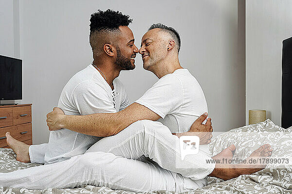 Romantic gay couple nuzzling on bed at home