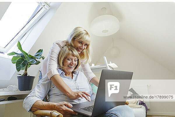 Happy blond woman with mother using laptop at home