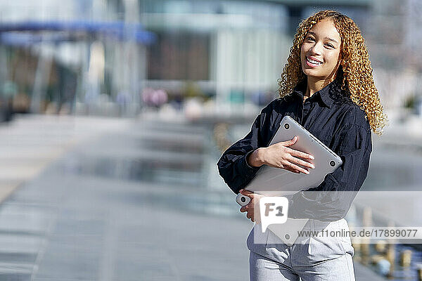 Happy young businesswoman standing with laptop on sunny day