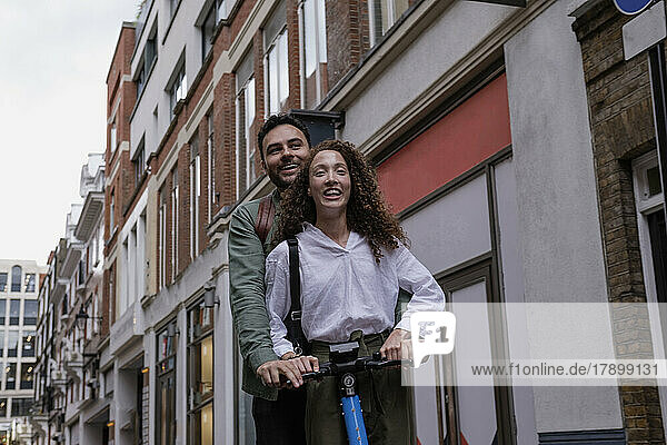 Happy couple riding electric push scooter in front of building