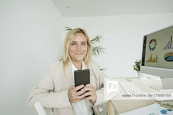 Smiling businesswoman using mobile phone at desk in office
