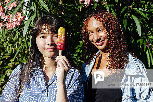 Smiling woman with friend holding ice cream standing in front of plant