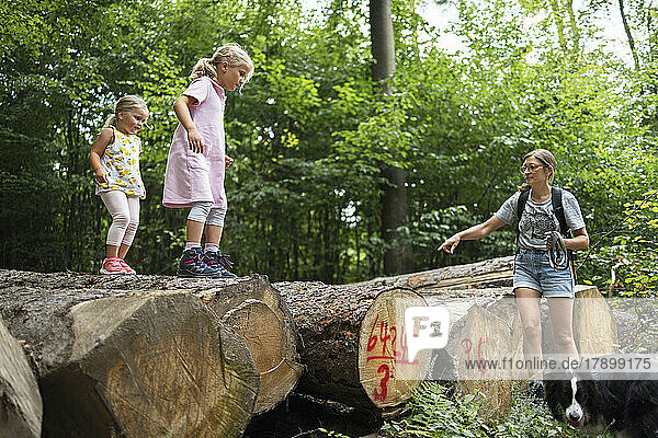 Mother guiding daughters to move down from fallen tree trunk in forest