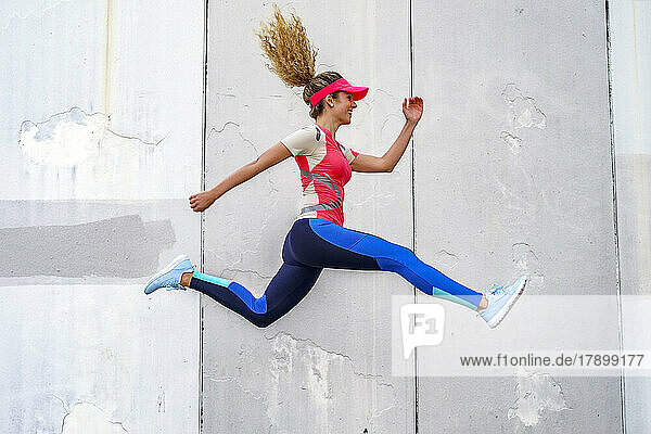 Happy sportswoman jumping in front of wall