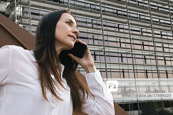 Mature businesswoman talking on smart phone in front of office building