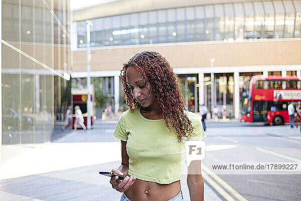 Junge Frau mit lockigem Haar  die Textnachrichten über das Smartphone sendet
