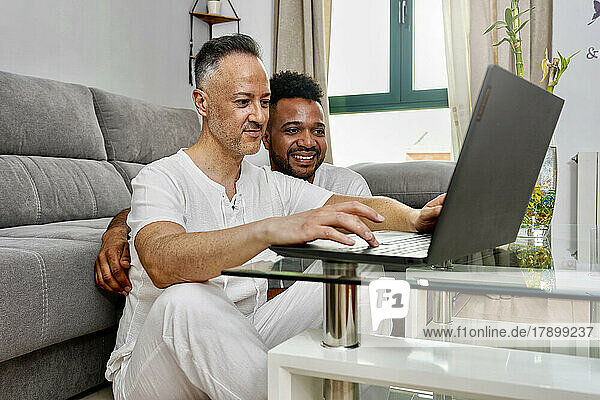 Homosexual couple using laptop sitting in living room at home