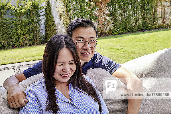 Lächelnder reifer Mann mit Brille neben Frau  die auf dem Sofa sitzt