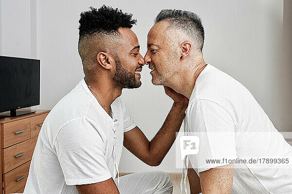 Romantic gay couple rubbing noses in bedroom