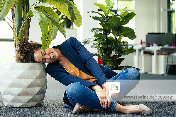 Mature businesswoman resting head on potted plant at workplace