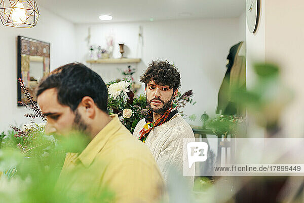 Thoughtful man standing with colleague at flower shop