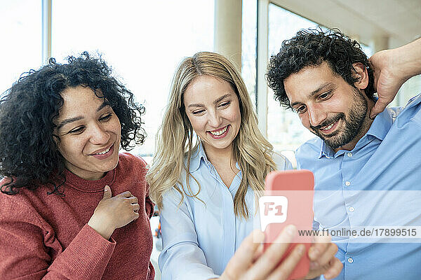 Smiling blond businesswoman taking selfie with colleagues on smart phone in office