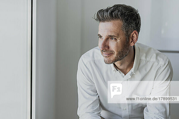 Smiling thoughtful businessman in front of white wall