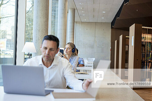 Reifer Professor arbeitet am Laptop am Schreibtisch in der Bibliothek