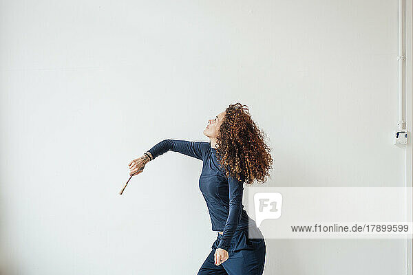 Woman with curly hair holding paintbrush in front of white wall