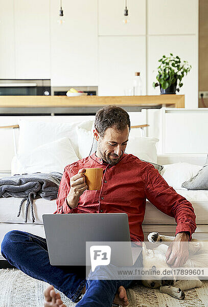 Freelancer sitting by dog holding coffee cup at home