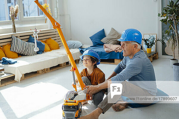 Großvater und Enkel tragen Schutzhelm und spielen zu Hause mit Spielzeugkran und Windturbinenmodell