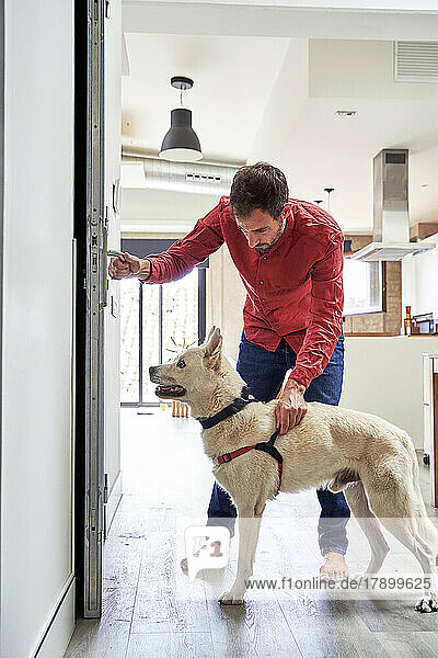 Mann hält Hund an der Leine und öffnet die Tür