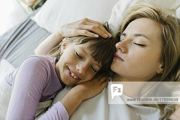 Smiling daughter sleeping with mother in bedroom