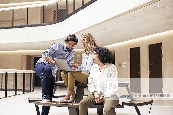 Smiling businesswoman discussing with colleagues over laptop in corridor