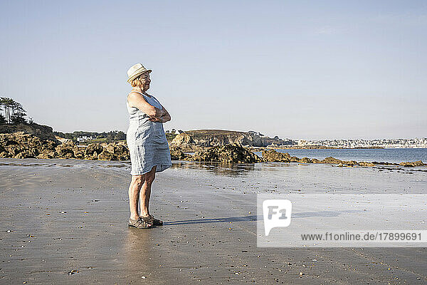 Senior woman with arms crossed standing at beach on sunny day