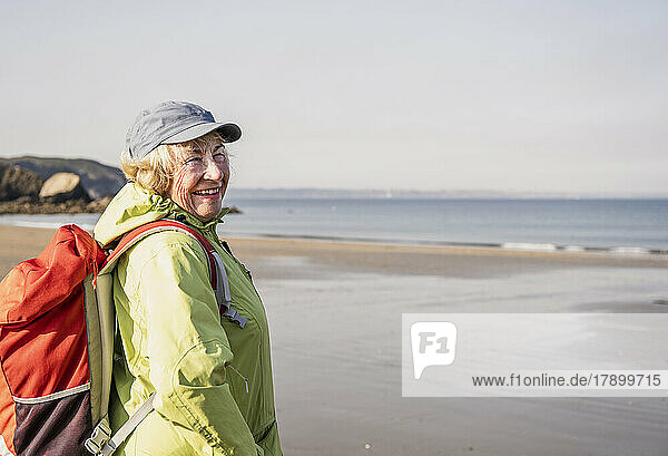 Happy senior woman with backpack standing at beach