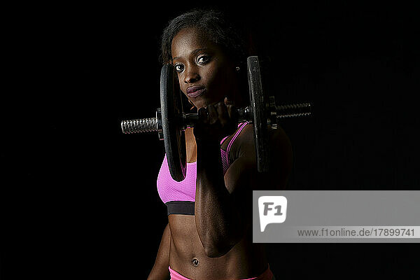 Confident athlete lifting dumbbell against black background