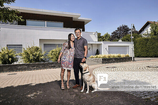 Happy mature couple with dog standing in front of house