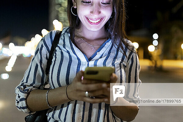 Happy woman surfing net through smart phone at night