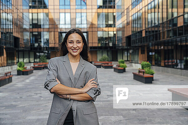 Happy confident businesswoman standing with arms crossed in front of office building