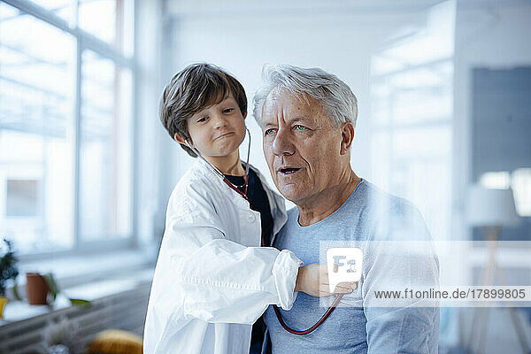 Grandson imitating as doctor checking grandfather with stethoscope at home