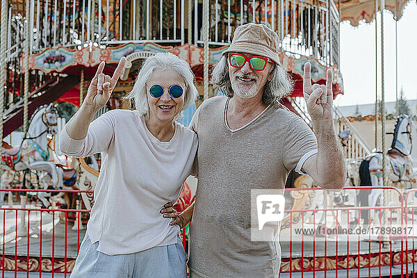 Glückliches Paar mit Sonnenbrille gestikuliert Hupenschild im Vergnügungspark