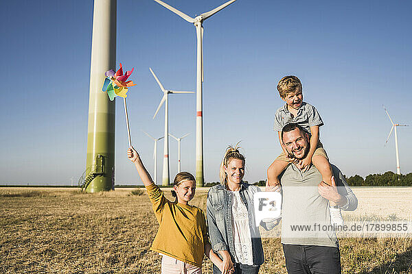 Optimistic family walking in wind park daughter carrying colorful pinwheel