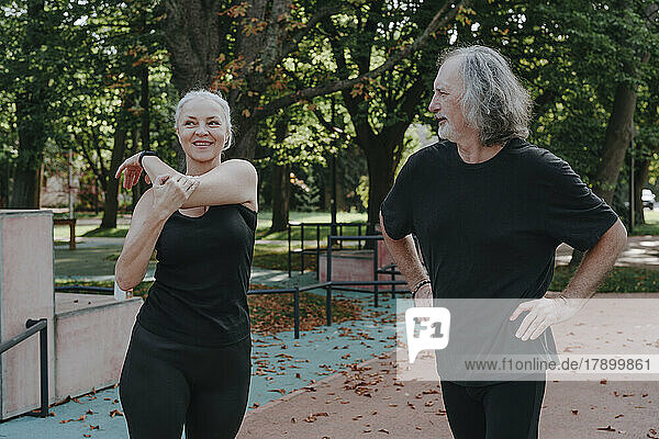 Mature woman with senior man doing stretching exercise in park