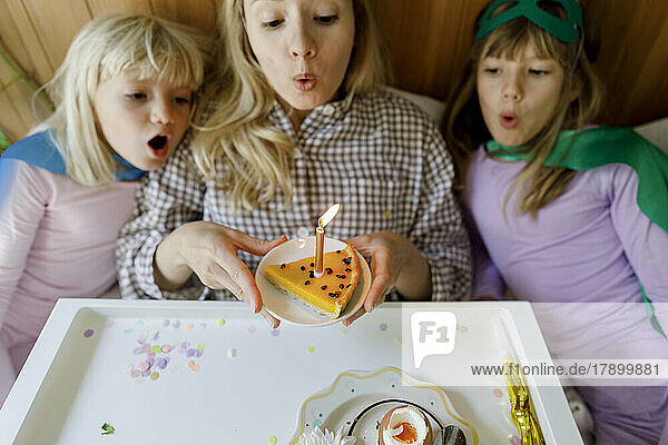 Mother with children blowing candle on cake at home