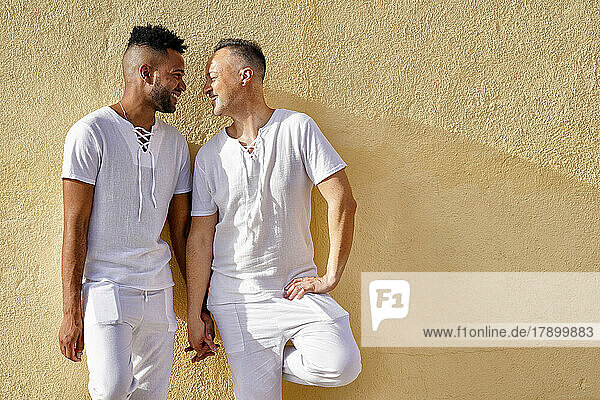 Fröhliches schwules Paar hält an einem sonnigen Tag Händchen vor der Wand