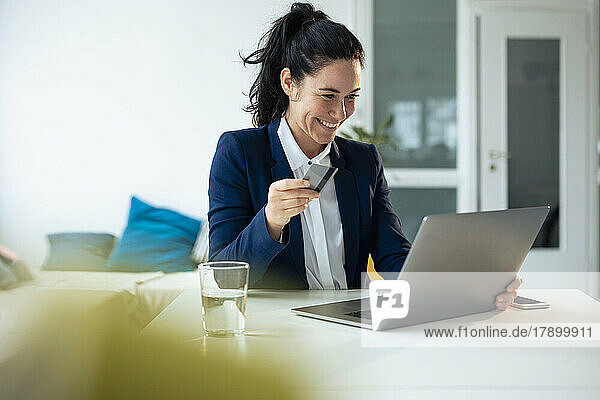 Happy businesswoman holding credit card doing online shopping through laptop