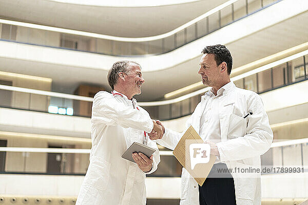 Doctor holding file shaking hand with colleague at hospital